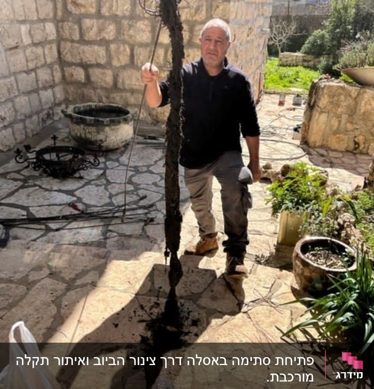 אדם מחזיק צינור עם לכלוך בחצר אבן